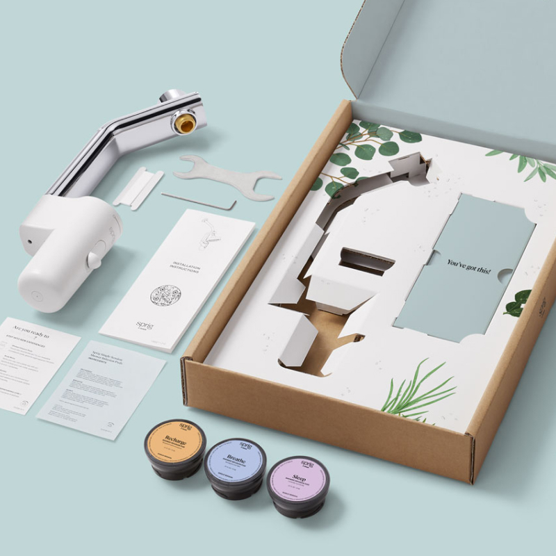 An open cardboard box showing the Shower Infusion Starter Kit, which includes the Sprig Shower Infusion Device, installation tools and three infusion pods.
